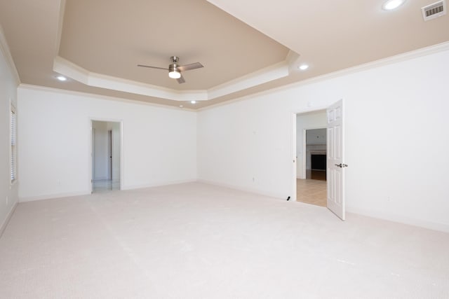 unfurnished room with ceiling fan, light colored carpet, ornamental molding, and a raised ceiling