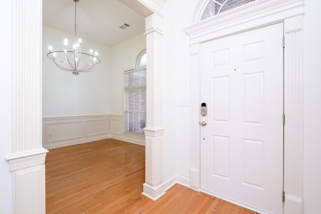 foyer with light hardwood / wood-style floors, a chandelier, ornamental molding, and ornate columns