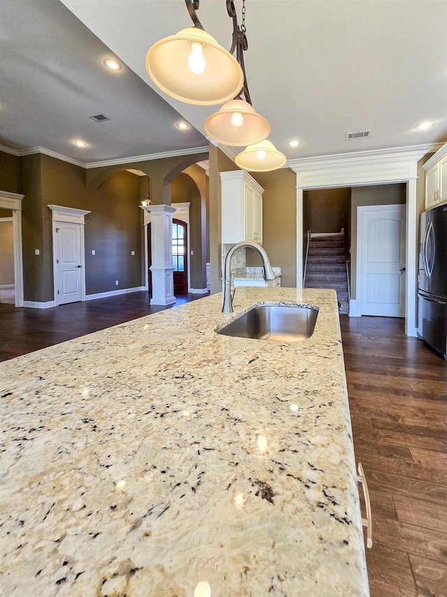 kitchen featuring sink, stainless steel refrigerator, hanging light fixtures, decorative columns, and light stone counters