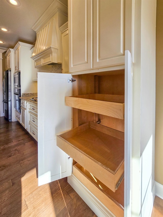 interior space with light stone countertops, premium range hood, appliances with stainless steel finishes, and dark hardwood / wood-style flooring