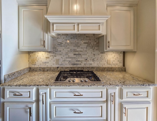 kitchen with light stone counters, decorative backsplash, stainless steel gas cooktop, and custom exhaust hood