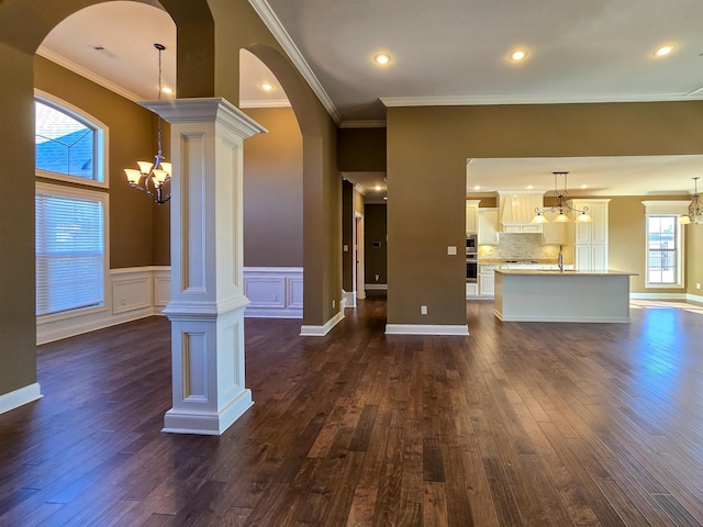 unfurnished living room with ornate columns, ornamental molding, dark wood-type flooring, and a notable chandelier