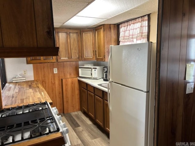 kitchen featuring wood walls, white appliances, light hardwood / wood-style flooring, and a drop ceiling