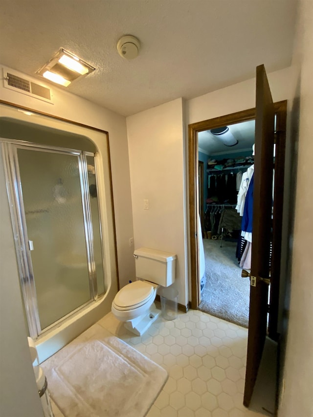 bathroom featuring a textured ceiling, toilet, and a shower with door