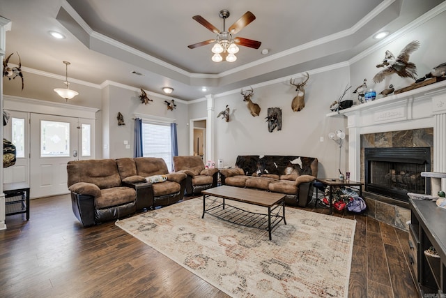 living room with crown molding, a tiled fireplace, a tray ceiling, and dark hardwood / wood-style flooring