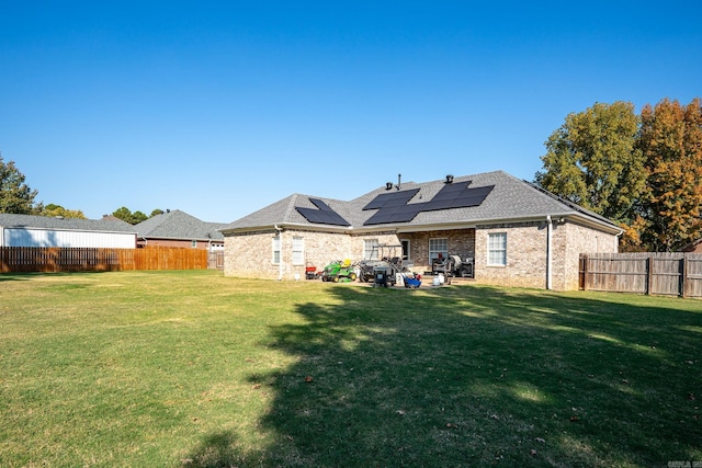 rear view of house featuring a lawn and solar panels