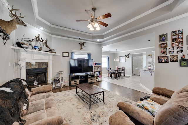 living room with crown molding, light hardwood / wood-style flooring, a raised ceiling, and a fireplace