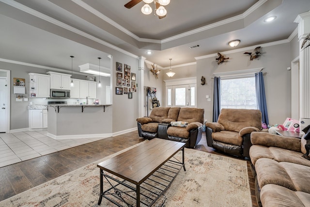 living room featuring light hardwood / wood-style floors, a raised ceiling, ornamental molding, and ceiling fan