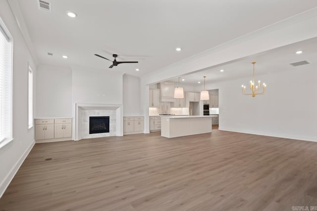 unfurnished living room with wood-type flooring, ceiling fan with notable chandelier, and crown molding