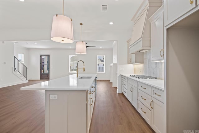 kitchen featuring pendant lighting, white cabinets, premium range hood, backsplash, and a kitchen island with sink