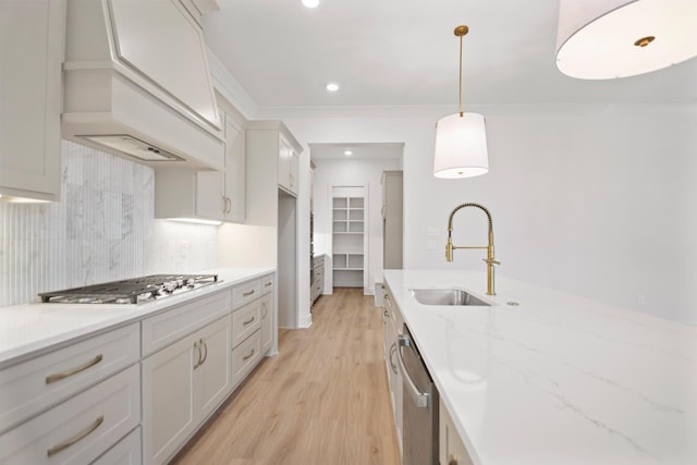 kitchen featuring appliances with stainless steel finishes, hanging light fixtures, sink, light hardwood / wood-style flooring, and backsplash