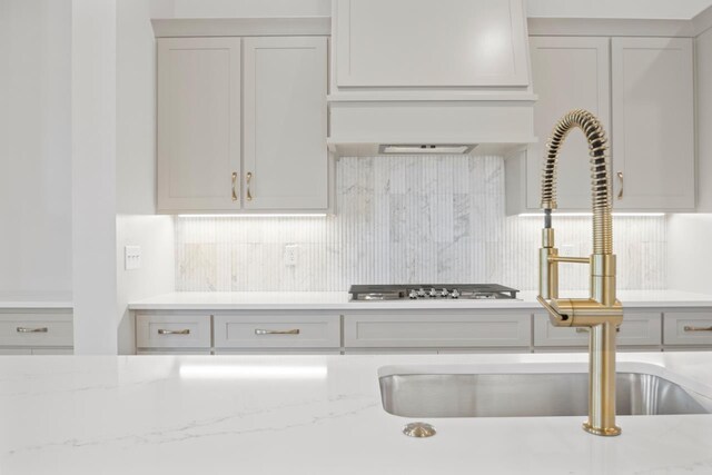 kitchen featuring sink, custom exhaust hood, backsplash, and light stone counters