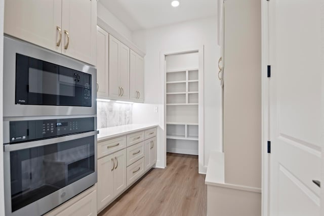 kitchen with stainless steel oven, built in microwave, tasteful backsplash, white cabinetry, and light hardwood / wood-style flooring