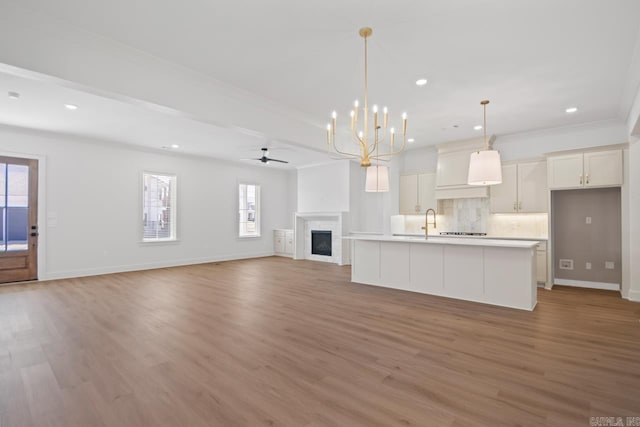 unfurnished living room with ceiling fan with notable chandelier, sink, hardwood / wood-style floors, and crown molding