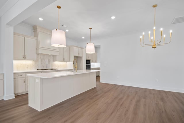 kitchen with pendant lighting, sink, hardwood / wood-style flooring, an island with sink, and decorative backsplash