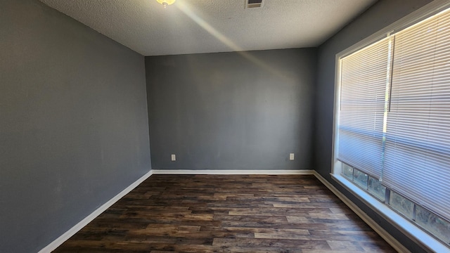 spare room featuring a healthy amount of sunlight, a textured ceiling, and dark hardwood / wood-style flooring