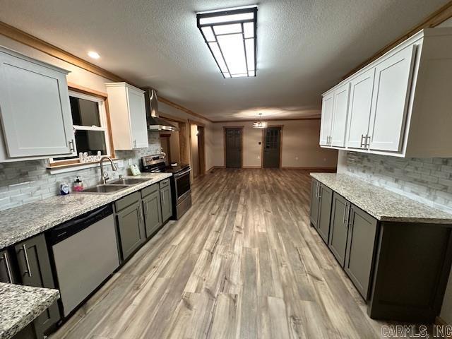 kitchen with light stone countertops, appliances with stainless steel finishes, white cabinetry, sink, and wall chimney range hood