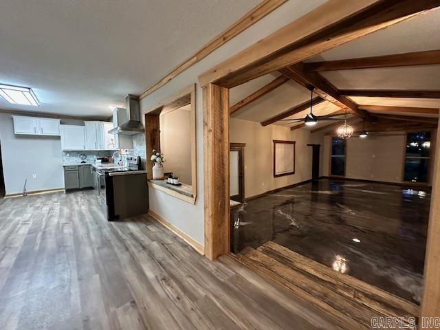 kitchen featuring white cabinetry, wall chimney range hood, backsplash, lofted ceiling with beams, and hardwood / wood-style flooring