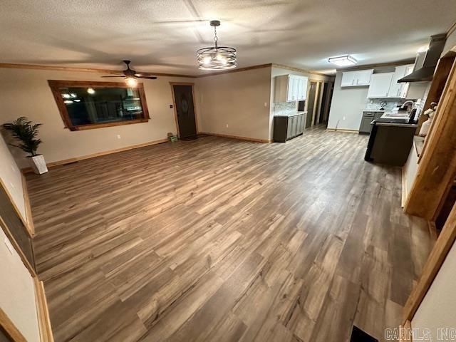 unfurnished living room with crown molding, ceiling fan, sink, hardwood / wood-style flooring, and a textured ceiling