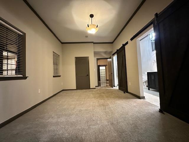 carpeted spare room featuring ornamental molding and a barn door