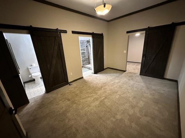 unfurnished bedroom featuring connected bathroom, a barn door, crown molding, and light carpet