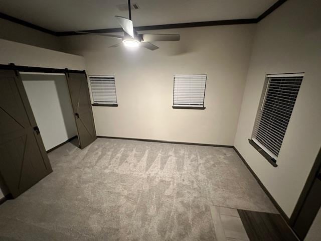 unfurnished bedroom featuring light carpet, ceiling fan, and a barn door