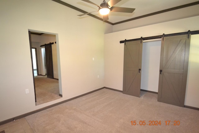 unfurnished bedroom with ceiling fan, light colored carpet, crown molding, and a barn door