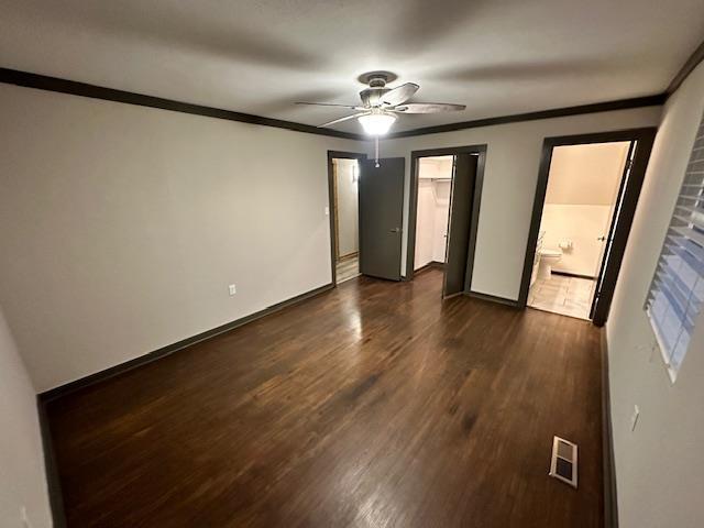 unfurnished bedroom featuring ceiling fan, dark wood-type flooring, ensuite bath, and ornamental molding