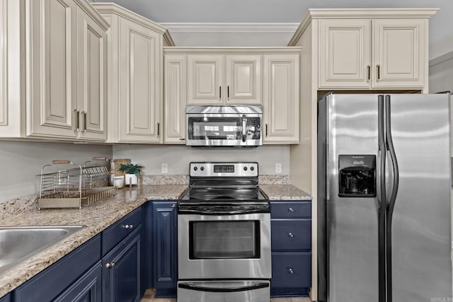 kitchen with blue cabinetry, ornamental molding, appliances with stainless steel finishes, light stone countertops, and cream cabinets