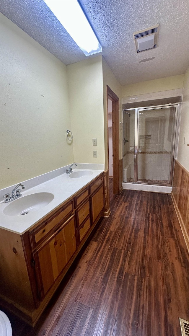 bathroom featuring hardwood / wood-style flooring, a shower with door, wooden walls, vanity, and a textured ceiling