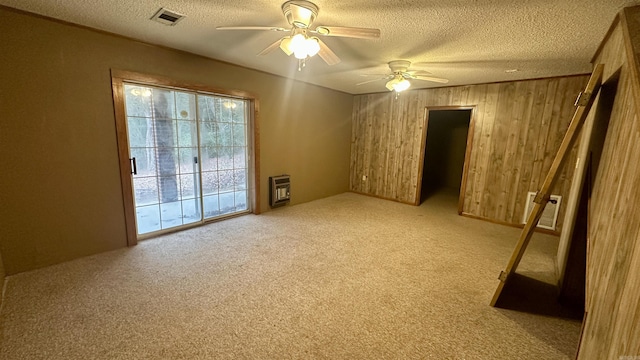 empty room with light carpet, heating unit, a textured ceiling, and wood walls