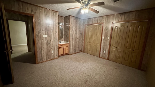 unfurnished bedroom featuring wooden walls, two closets, a textured ceiling, and ceiling fan