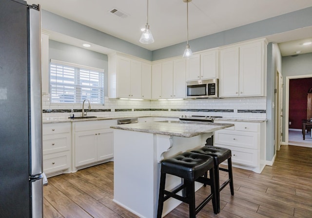 kitchen featuring sink, appliances with stainless steel finishes, white cabinetry, a center island, and a kitchen bar