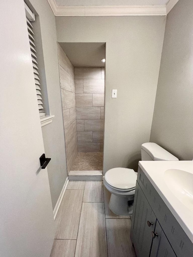 bathroom featuring crown molding, a tile shower, vanity, and toilet