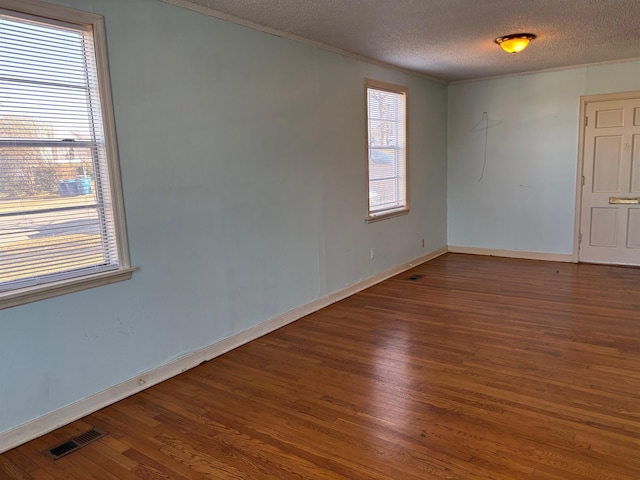 unfurnished room featuring visible vents, baseboards, ornamental molding, wood finished floors, and a textured ceiling