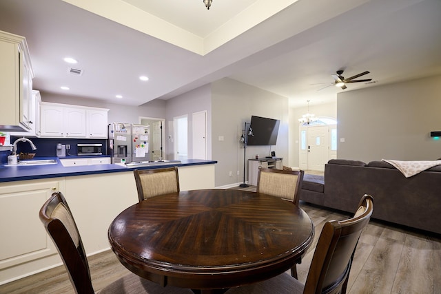 dining room with ceiling fan with notable chandelier, light hardwood / wood-style floors, and sink