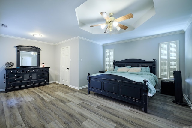 bedroom featuring wood-type flooring, ornamental molding, a raised ceiling, and ceiling fan