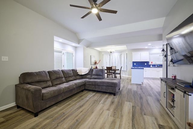 living room featuring lofted ceiling, sink, ceiling fan with notable chandelier, and light wood-type flooring