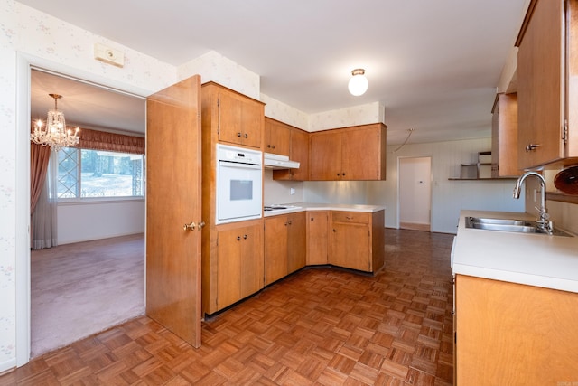 kitchen with parquet flooring, pendant lighting, stovetop, sink, and oven