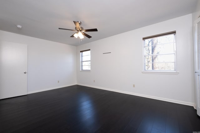 spare room featuring dark wood-type flooring, a ceiling fan, and baseboards