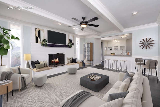 living area featuring ceiling fan, ornamental molding, beamed ceiling, and a brick fireplace