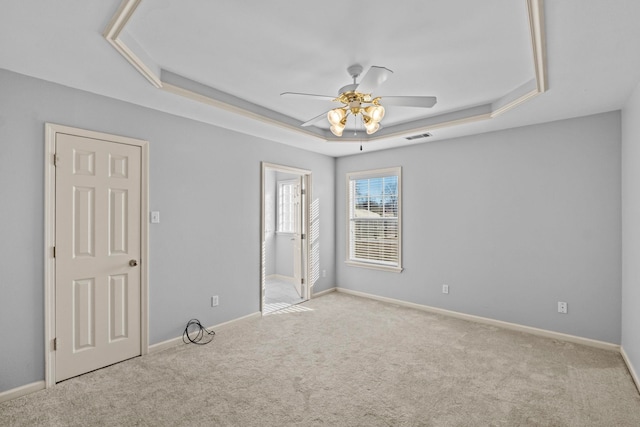 unfurnished room featuring light carpet, a tray ceiling, and ceiling fan