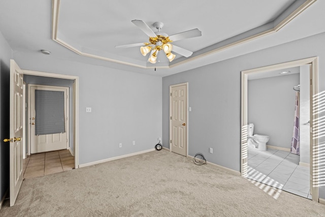 unfurnished bedroom with ensuite bath, light colored carpet, a tray ceiling, a closet, and ceiling fan