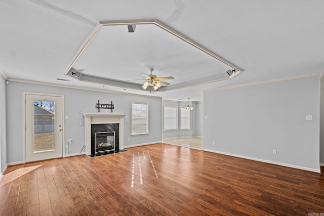 unfurnished living room featuring crown molding, a tray ceiling, a high end fireplace, light hardwood / wood-style floors, and ceiling fan with notable chandelier