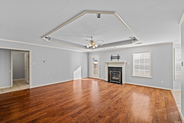 unfurnished living room featuring crown molding, a high end fireplace, a raised ceiling, and ceiling fan