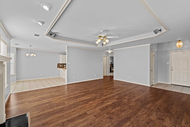 unfurnished living room with ceiling fan with notable chandelier, light hardwood / wood-style floors, and a tray ceiling