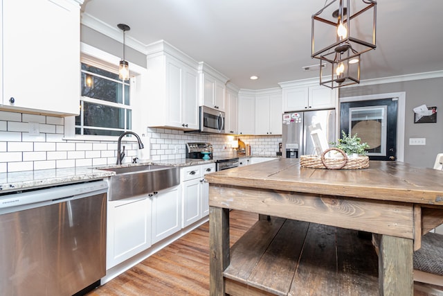 kitchen with appliances with stainless steel finishes, decorative light fixtures, white cabinetry, sink, and light stone counters