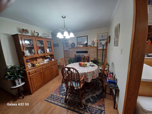 dining space featuring an inviting chandelier, crown molding, a stone fireplace, and light wood-type flooring