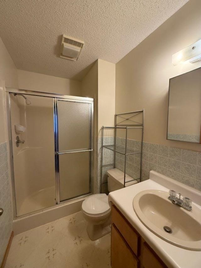 bathroom with tile walls, a textured ceiling, toilet, and walk in shower