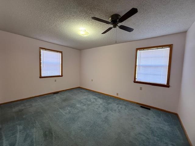 carpeted spare room with ceiling fan, a healthy amount of sunlight, and a textured ceiling